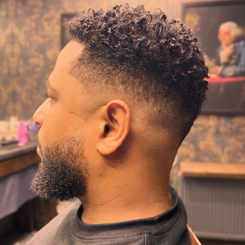 A skilled barber in Krakow expertly cutting a client's tight curly hair with clippers and a comb.